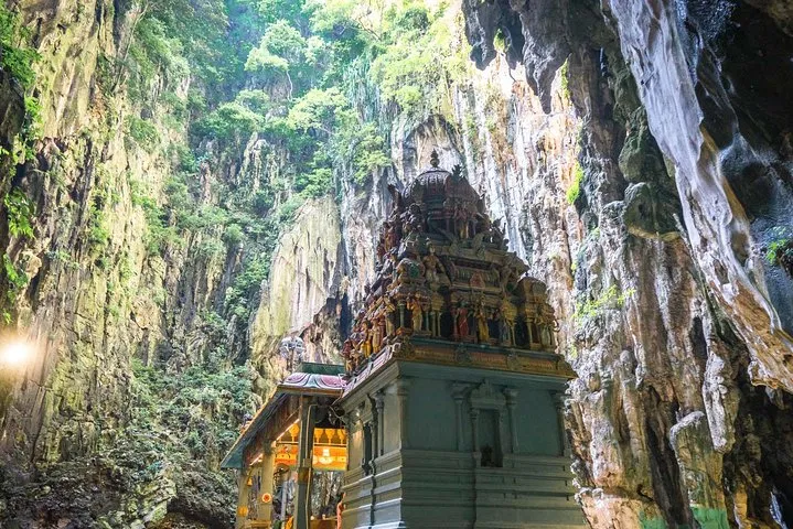 A gopuram-topped shrine standing under the open limestone chamber of the Temple Cave